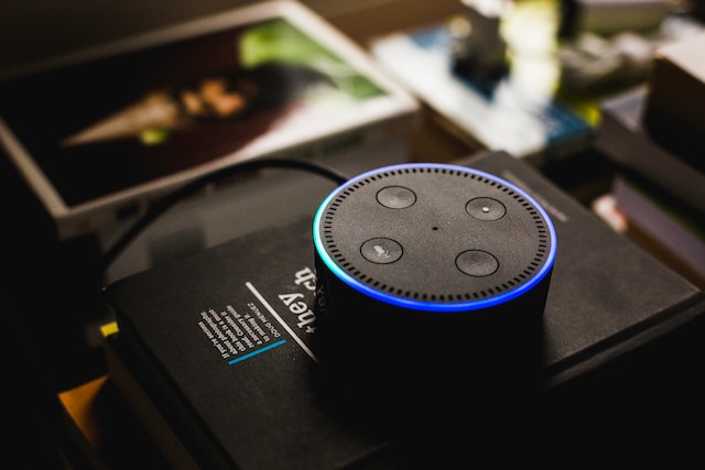 an amazon echo dot lit up blue on top a pile of books
